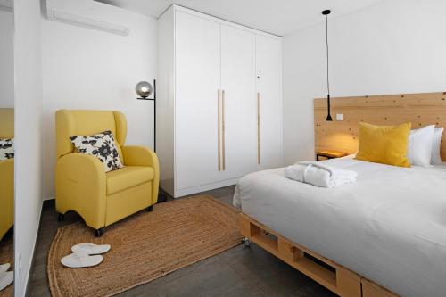 ein Schlafzimmer mit einem Bett und einem gelben Stuhl in der Unterkunft Rocha do Mar 1 in Biscoitos