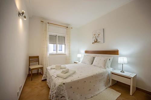 a white bedroom with a bed and a chair at Casa Bege T2 in Burgau