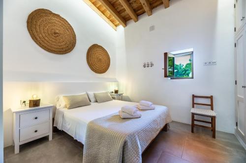 a white bedroom with a bed and a chair at Can Xumeu Ferrer in La Mola