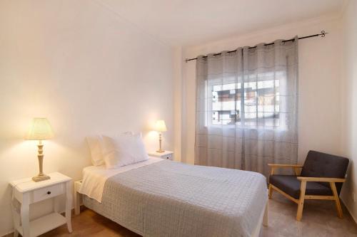 a bedroom with a bed and a chair and a window at Âncora B in Monte Gordo