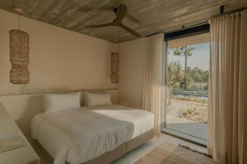 a bedroom with a bed with a ceiling fan and a window at M Villa Comporta Retreat in Carvalhal