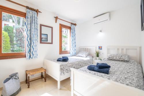two beds in a white room with blue curtains at Can Botana 10 in Cala de Sant Vicenc