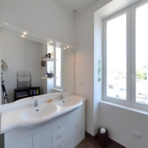 a white bathroom with a large mirror and a sink at Gîtes du Parc in Vallon-Pont-dʼArc