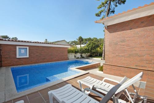 a swimming pool with white chairs next to a brick building at Moradia Pinheiro Manso in Apúlia