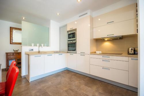 a kitchen with white cabinets and a red chair at Bergantin 7 in Port de Pollensa
