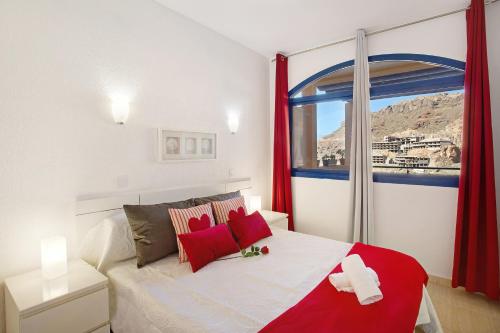 a bedroom with a bed with red curtains and a window at Paraiso Playa Taurito in Taurito