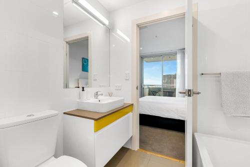 a white bathroom with a sink and a bed at Adelaide Central Skyline Panoramic Suite Three in Adelaide