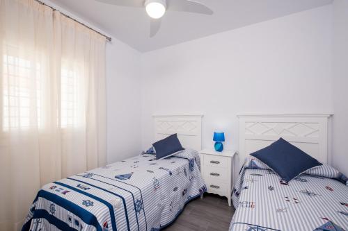 two beds in a bedroom with white walls and blue pillows at Casa El Palmar 2 in Vejer de la Frontera