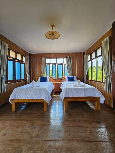 two beds in a room with windows at ฮักจังโฮมสเตย์ ที่พักแม่แตง in Chiang Mai