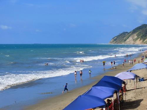 a group of people on a beach with blue umbrellas at Hotel Puerto Ballesta in Tonsupa