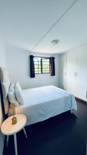 a white bedroom with a large bed and a table at Badumetsie cottage in Durban