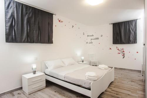 a white bedroom with a white bed and flowers on the wall at Villetta farfalle in Sarroch