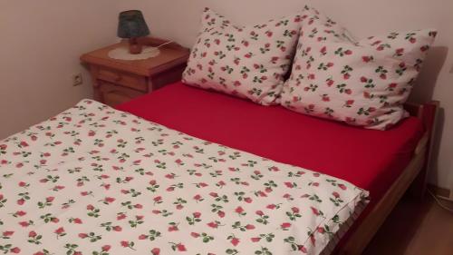a bed with a red sheet with flowers on it at Ferienwohnung Schmidt in Krummhörn