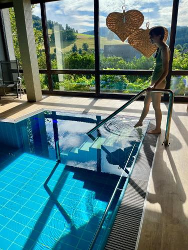 a woman holding an umbrella standing next to a swimming pool at B&B Apart Hotel Goldener Hahn - Pool & Sauna, Frühstück in Baiersbronn