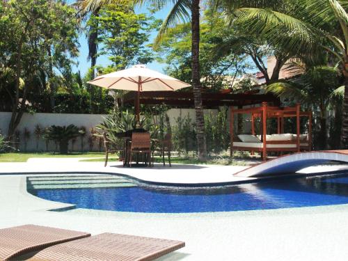 uma piscina com um guarda-sol, uma mesa e cadeiras em Hotel Boutique Recanto da Passagem em Cabo Frio