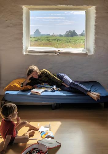 a woman laying on a bed under a window at L'ancien Gonio de l'Île in Lampaul