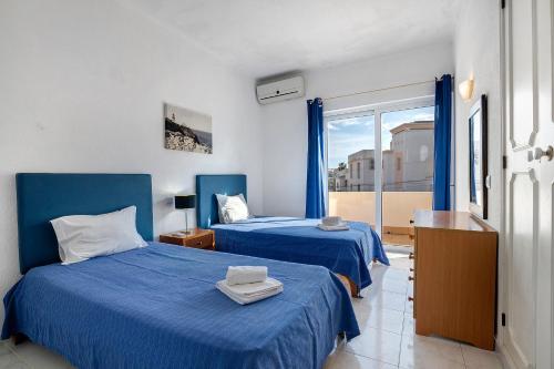 two beds in a room with blue sheets and a window at Villa Martins in Albufeira