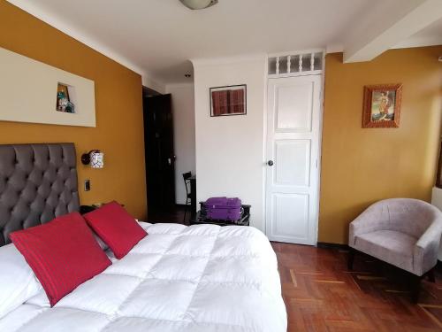 a bedroom with a white bed with red pillows and a chair at Hotel Juan in Arequipa