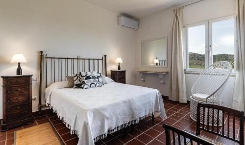 a bedroom with a bed and a chair and a window at Villa Aquila Giardino in Is Molas 
