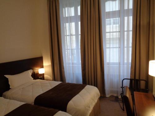 a hotel room with two beds and two windows at Hotel de Montaulbain in Verdun