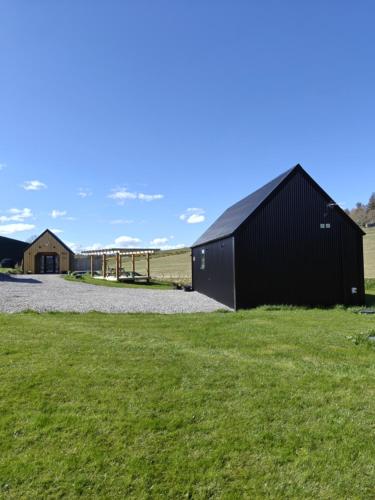 a black building in a field with green grass at Temuka Lodge in Glenurguhart