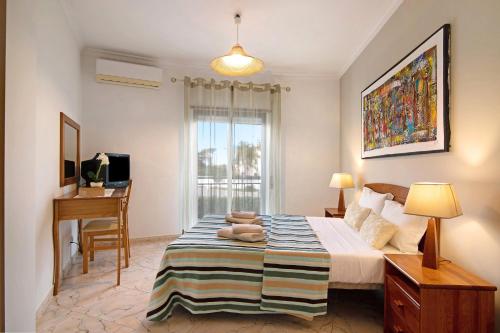 a bedroom with a bed with a desk and a window at Columbus Beach Apartment in Quarteira