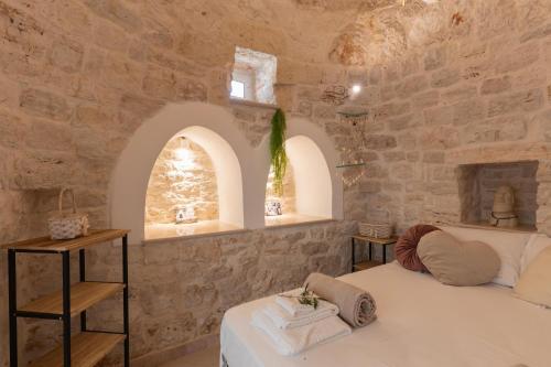 a bedroom with a white bed in a stone wall at Trulli Aletheia Con Piscina Privata in Ceglie Messapica