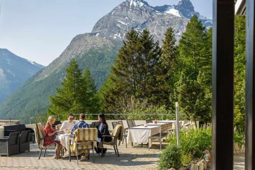 a group of people sitting at a table with mountains in the background at Waldhotel Fletschhorn Private Whole Hotel in Saas-Fee 360 Alpine Views & Sauna in Saas-Fee