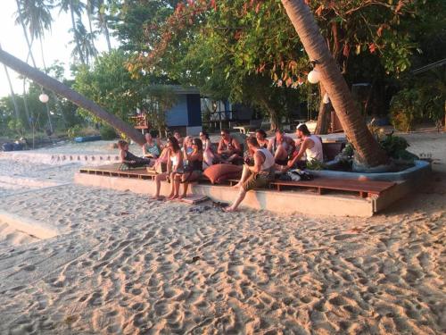een groep mensen die op bankjes op het strand zitten bij Two Rocks Bungalows in Baan Tai