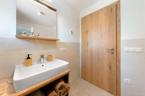 a bathroom with a white sink and a wooden door at Töniglerhof Apt Abendrot in Trodena