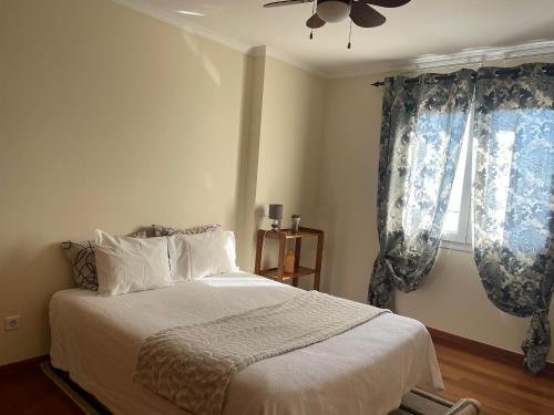 a bedroom with a bed with blue curtains and a ceiling fan at Apartamento Jade in Caniço