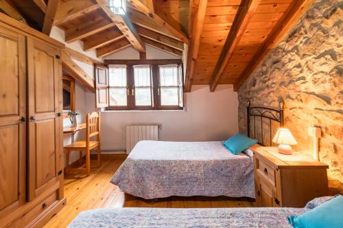 a bedroom with two beds in a room with a stone wall at Casa Rural Perullé in San Vicente de la Barquera