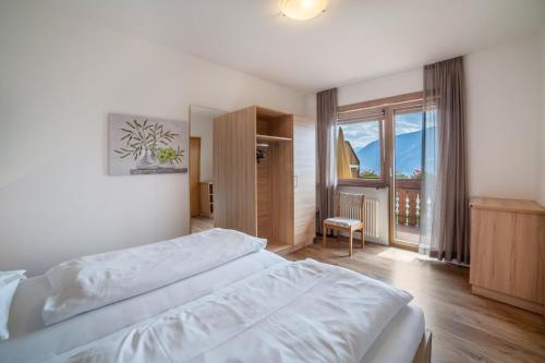 a bedroom with a white bed and a large window at Gartenheim App Maria in Schenna
