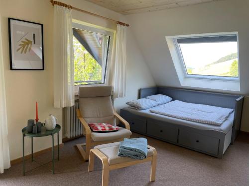 a bedroom with a bed and a chair and two windows at Gullerhof Ferienwohnung - Köpfle in Glottertal