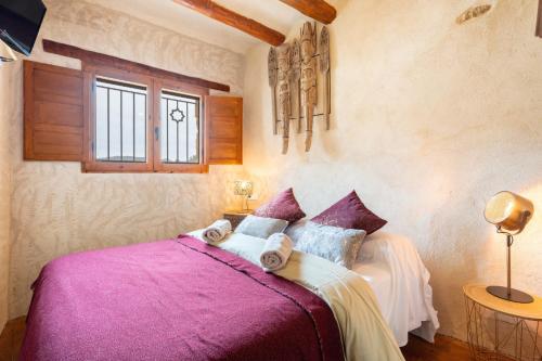 a bedroom with a bed with purple sheets and a window at El Kubo in Olba