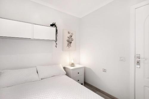 a white bedroom with a bed and a night stand at Las Teresitas Beach Apartment in San Andrés