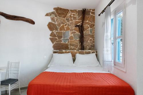 a bedroom with a red bed with a stone wall at Politimis Studio N1 in Amorgos