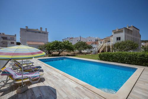 a swimming pool with two chairs and an umbrella at Villas Brites nº4 in Burgau