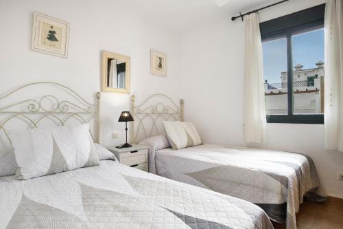a white bedroom with two beds and a window at Bella Vistas in Zahara de los Atunes