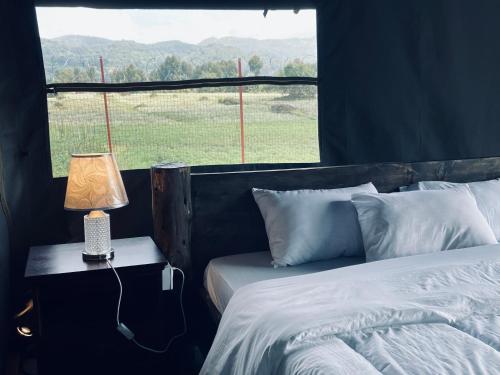 a bed with a lamp on a table next to a window at Volcanoes Over View Safaris & Camp in Nyarugina