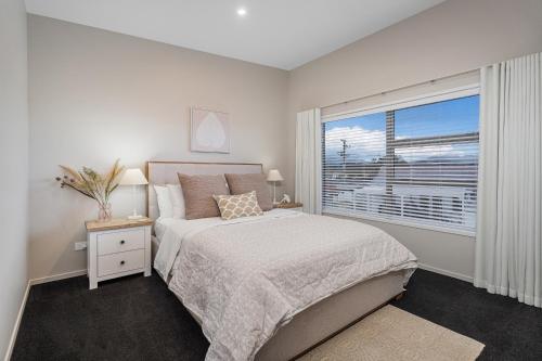a white bedroom with a bed and a window at Wharf Landing - Harbour View with Sunny Balcony, Walk to Town in Coromandel Town