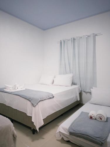 two beds in a room with white walls and curtains at Pousada Descanso Do Preguiça in Barreirinhas