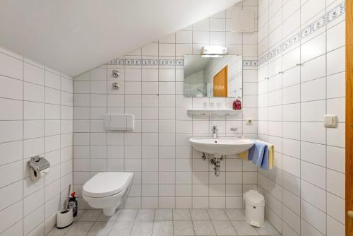 a white tiled bathroom with a toilet and a sink at Fewo Brünnstein - Nr 60 Pool, Sauna in Oberaudorf