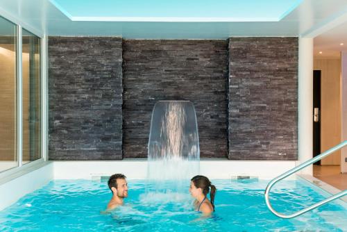 un hombre y una mujer en una bañera de hidromasaje con una cascada en Domaine de Cicé-Blossac, Resort Spa & Golf, en Bruz