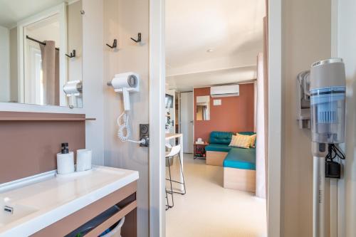 a bathroom with a sink and a room with a couch at Mh sympa au camping domaine la yole in Vendres