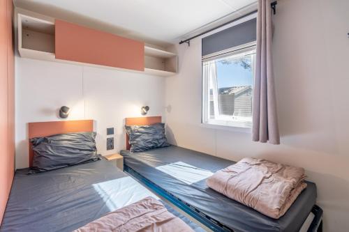 two beds in a room with a window at Mh sympa au camping domaine la yole in Vendres
