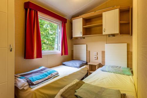 two beds in a small room with a window at Mobilehome au bord de l'eau in Gastes