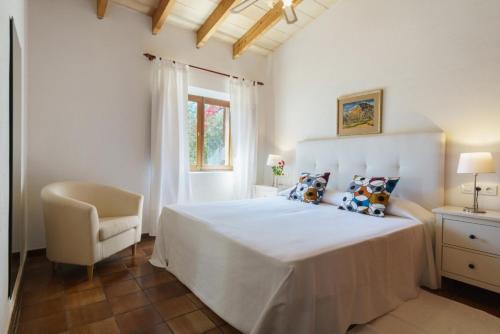 a white bedroom with a large bed and a chair at Llangana in Pollença
