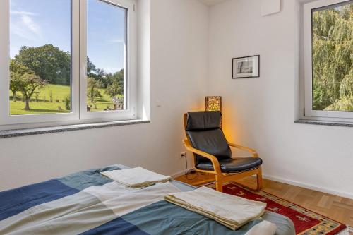 a bedroom with a chair and a bed and windows at Studio im Grünen und Bodenseenähe in Rielasingen-Worblingen