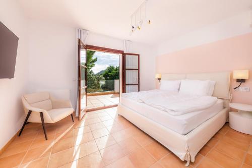 a white bedroom with a bed and a chair at Villa Font de sa Cala in Font de Sa Cala